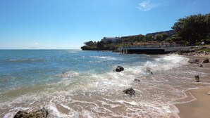 A beach with waves, a pier, and buildings in the background. - Tanjung Kodok Beach Resort (Paciran)