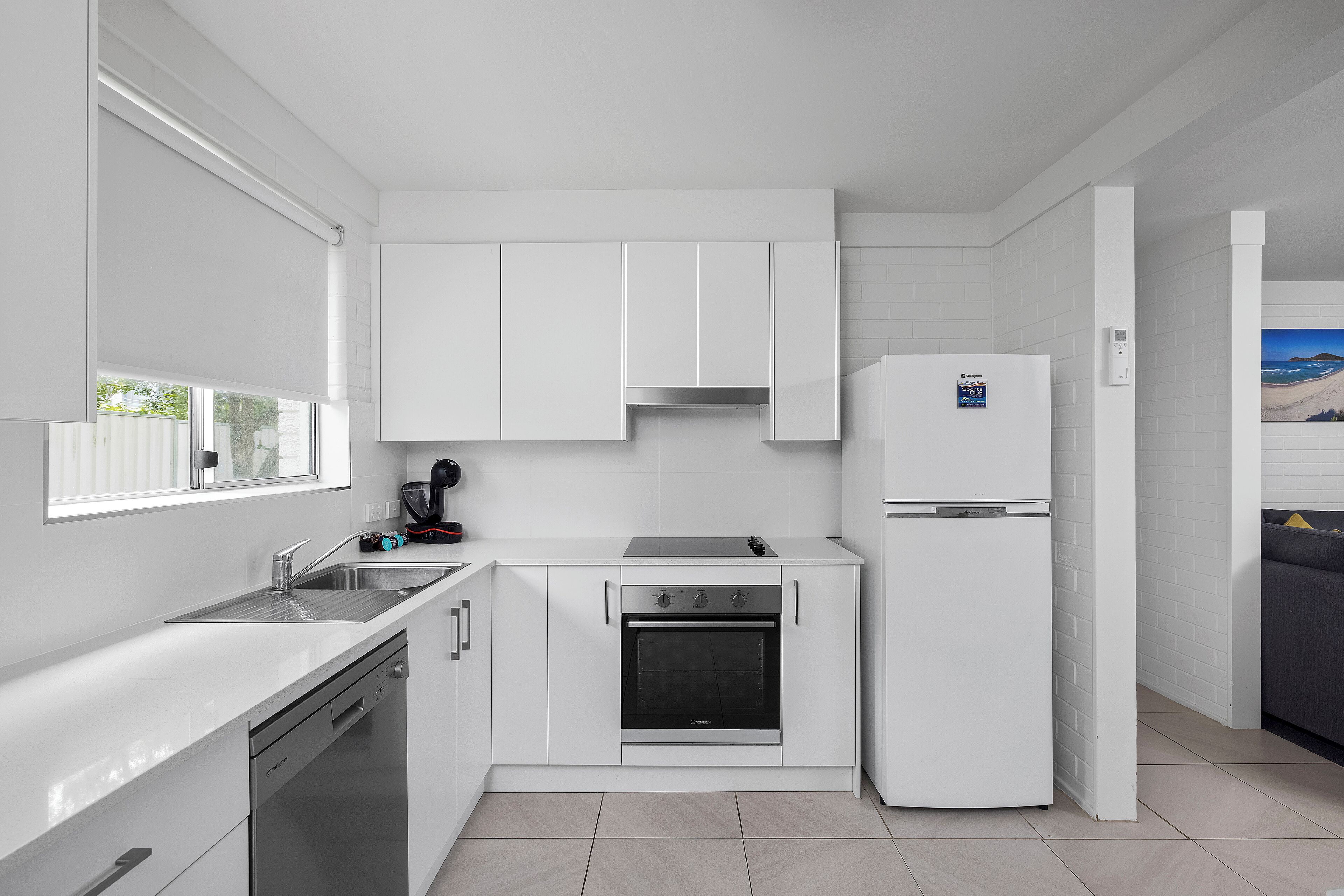 Una cocina compacta con muebles blancos, horno integrado y refrigerador.