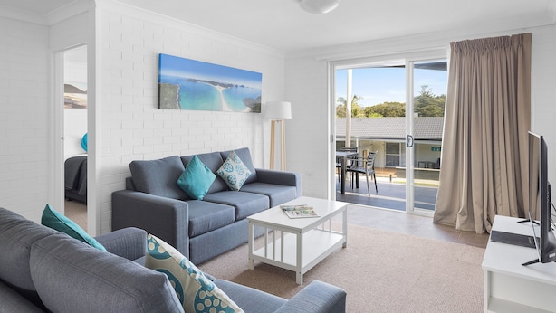 A modern living room with a grey sofa, a white coffee table, and a painting of a beach scene. - Seaside Holiday Resort Fingal Bay (Fingal Bay)