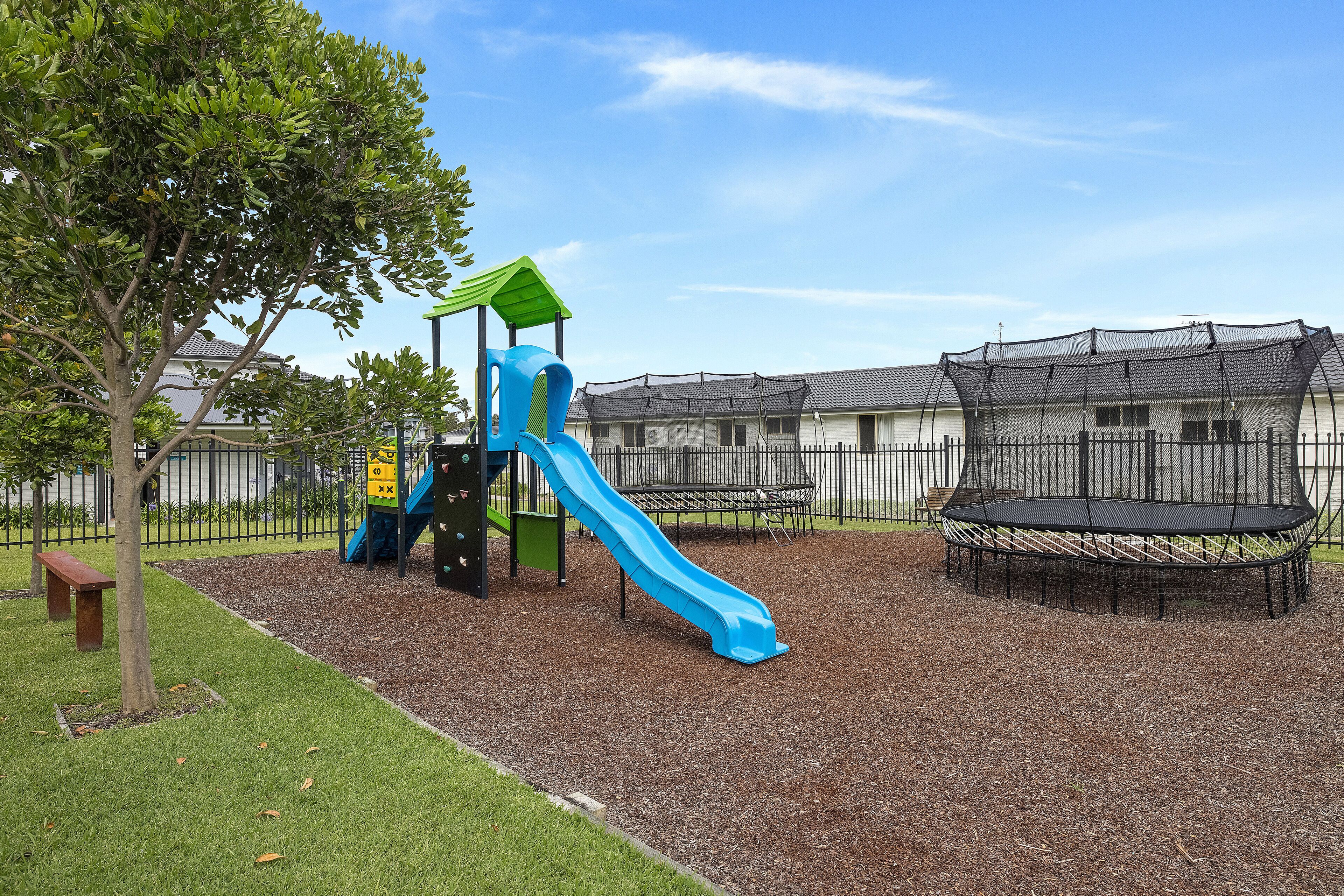 A playground with a blue slide, a green climbing structure, and a trampoline.