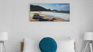 A bedroom with a bed, white pillows, a teal accent pillow, and a wall-mounted picture of a beach scene. - Seaside Holiday Resort Fingal Bay (Fingal Bay)
