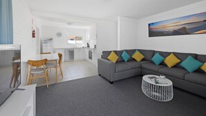 A modern living room with a grey sofa, wooden chairs, a white coffee table, and a painting on the wall. - Seaside Holiday Resort Fingal Bay (Fingal Bay)