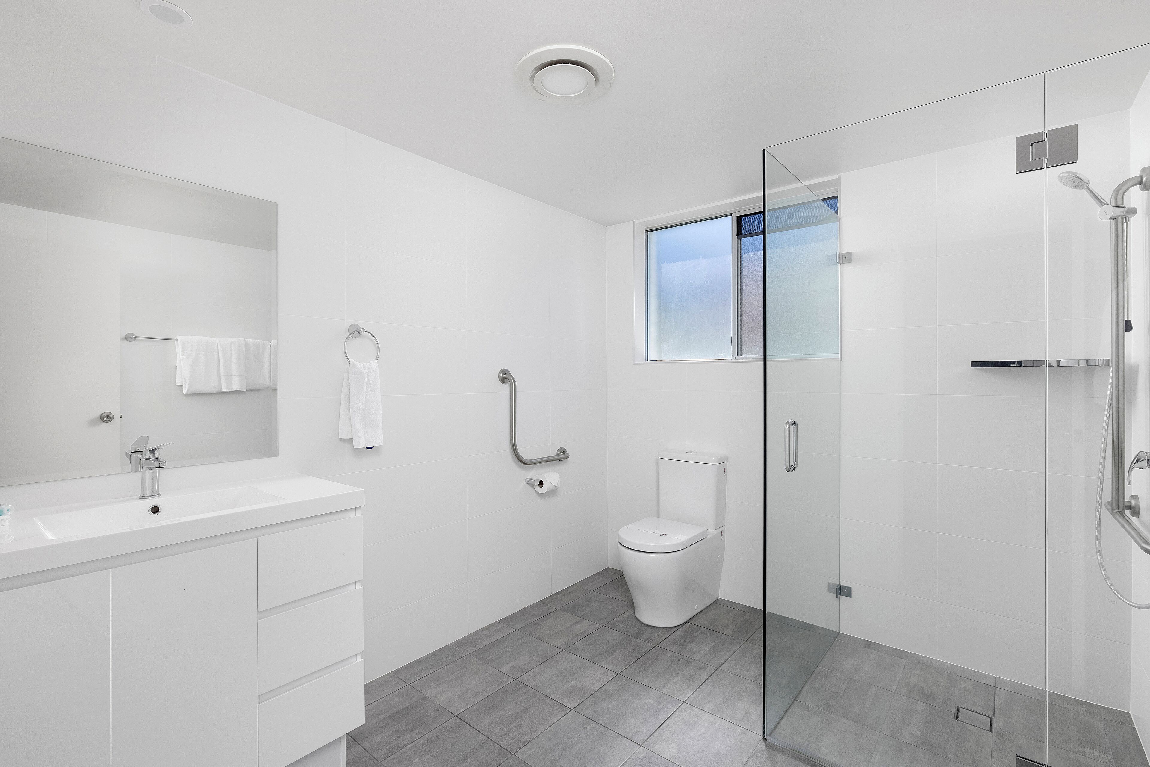 Un baño moderno con cabina de ducha de vidrio, un lavabo blanco y un inodoro.