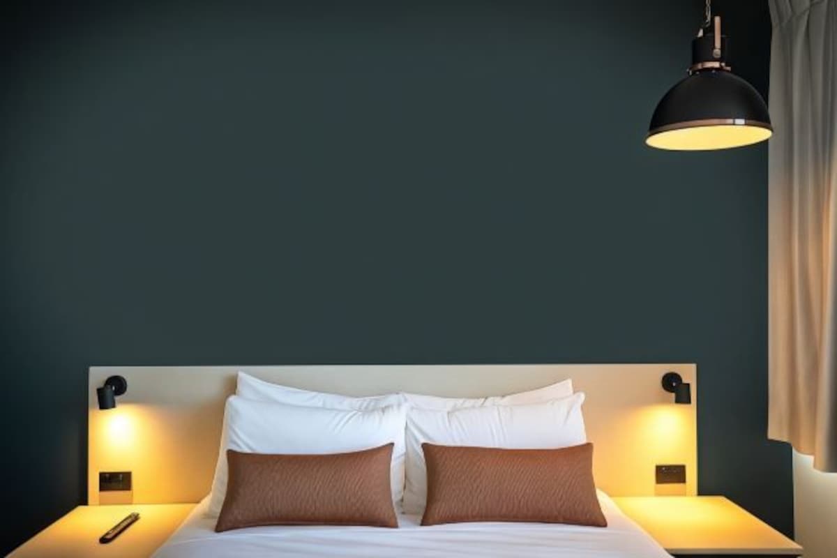 A hotel room with a bed, two bedside lamps, and a hanging light fixture.
