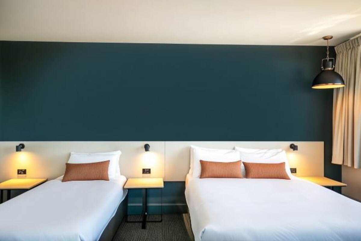 A hotel room with two single beds, each with a bedside table and lamp.