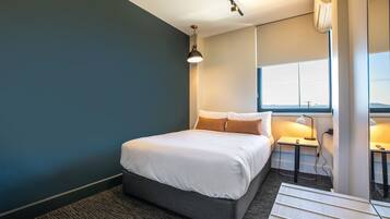 Una habitación de hotel moderna con una cama grande, mesitas de noche, una lámpara y un ventanal con vistas.