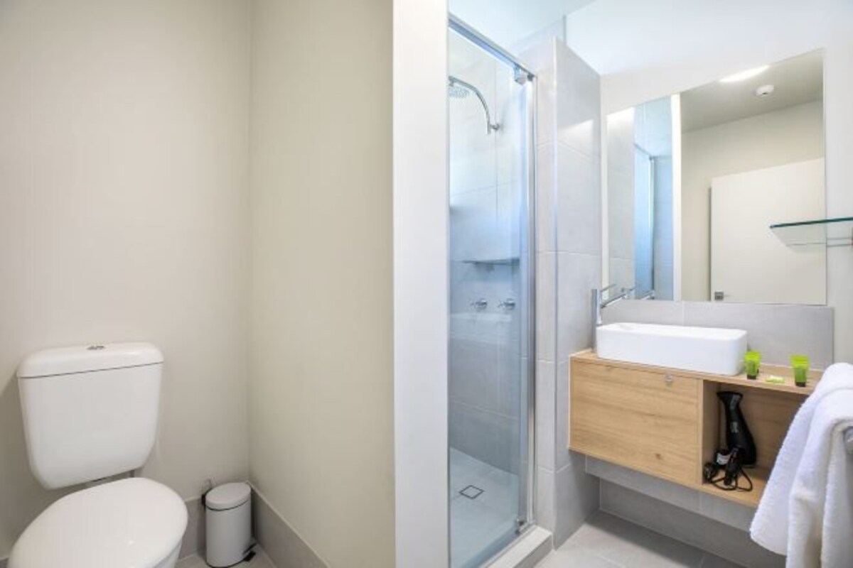 A modern bathroom with a toilet, a glass shower enclosure, a sink with a mirror, and a towel rack.