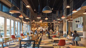 A spacious cafeteria with long communal tables, colorful chairs, and pendant lighting. - Atura Adelaide Airport (Adelaide Airport)