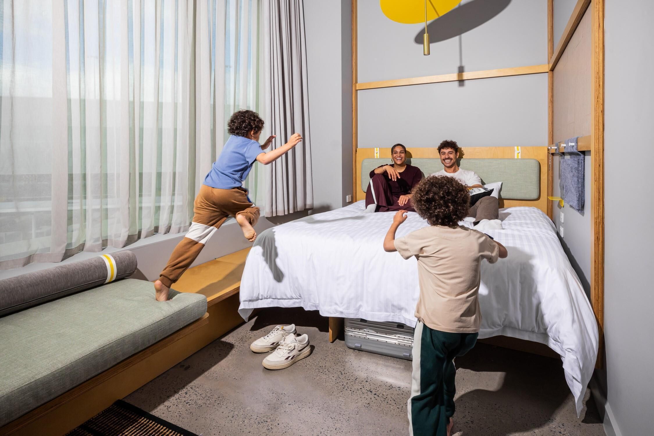A modern hotel room with a bed, a sofa, and a child playing.