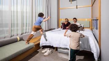 A modern hotel room with a bed, a sofa, and a child playing.