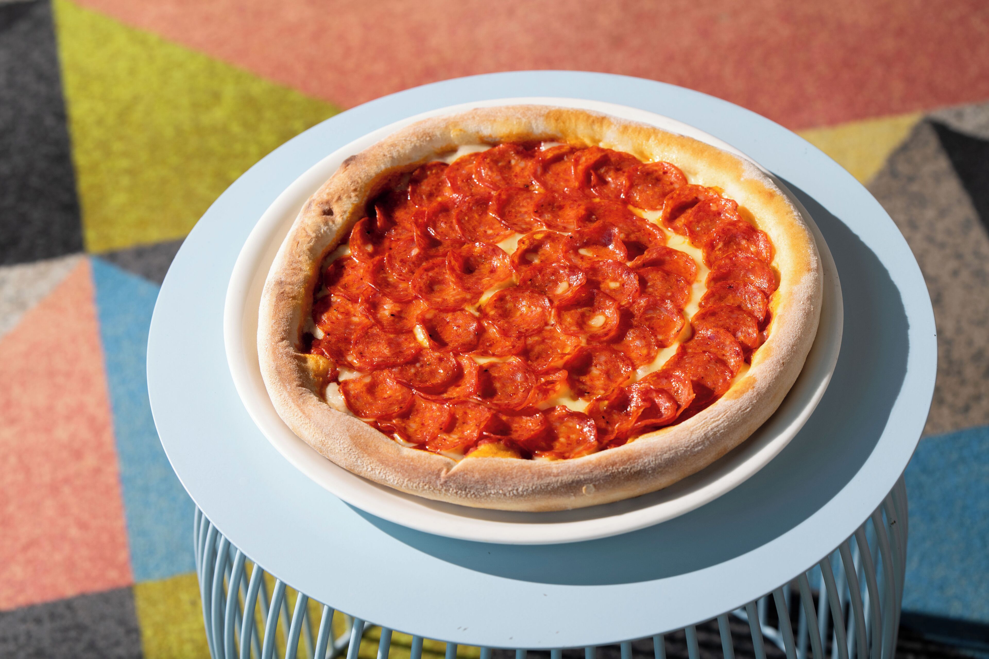 A pepperoni pizza on a white plate on a blue table.