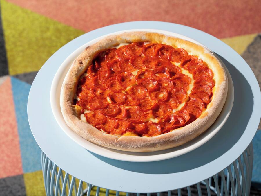 A pepperoni pizza on a white plate on a blue table.