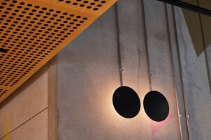 Un interior moderno con techo de madera perforada, pared de concreto y una lámpara circular.