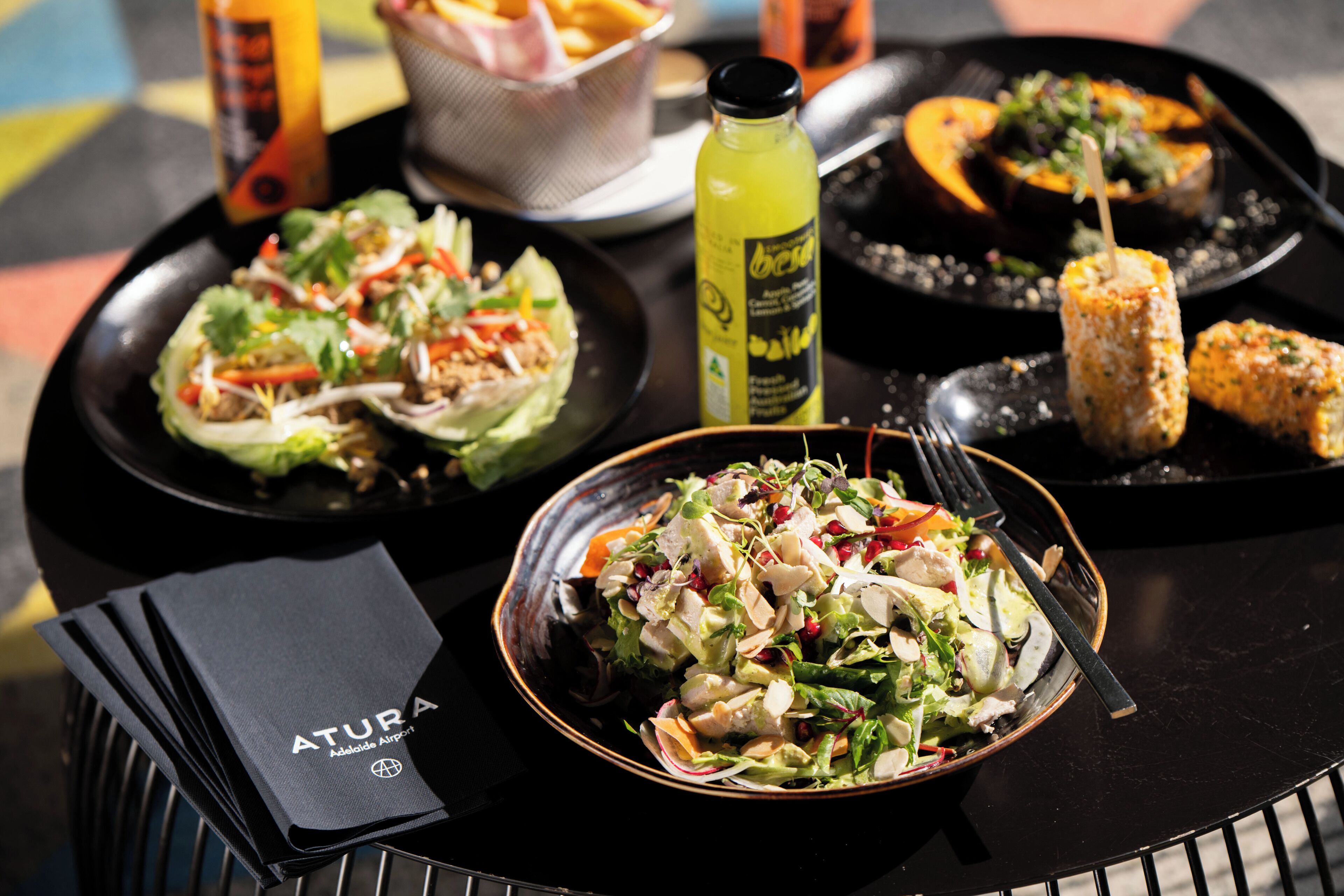 A table with various dishes including a salad, a bowl of food, and a bottle of drink.