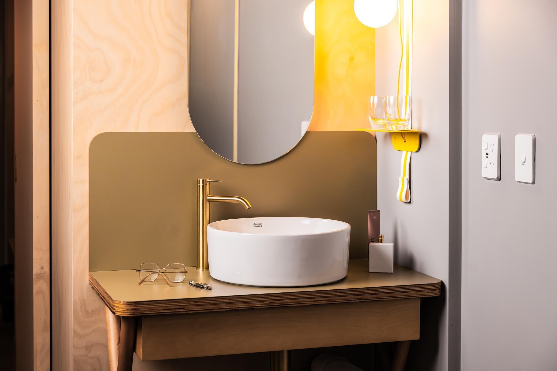 A modern bathroom with a round white sink, gold faucet, and a large mirror.