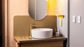 A modern bathroom with a round white sink, gold faucet, and a large mirror.