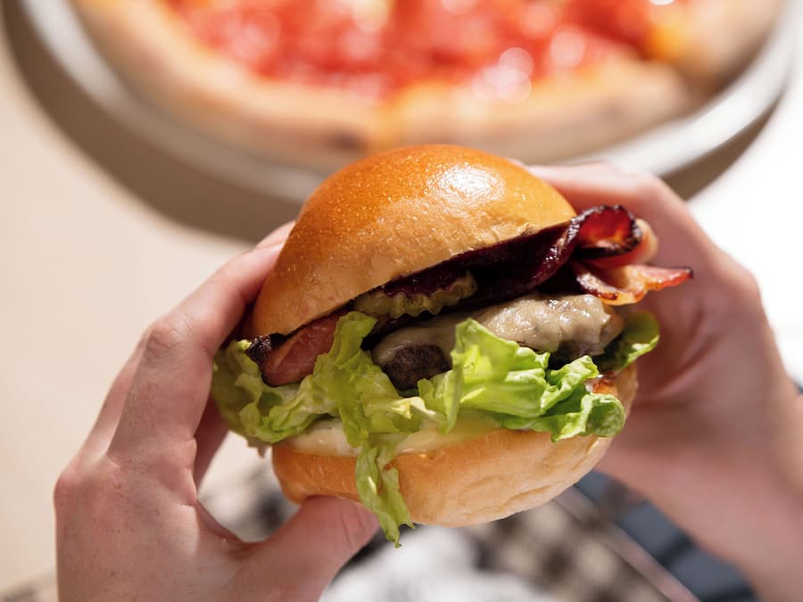 A person holding a burger with lettuce, bacon, and a bun.