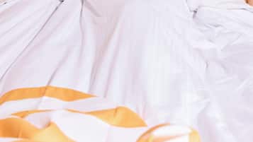 A bed with white bedding and a yellow and white striped blanket.