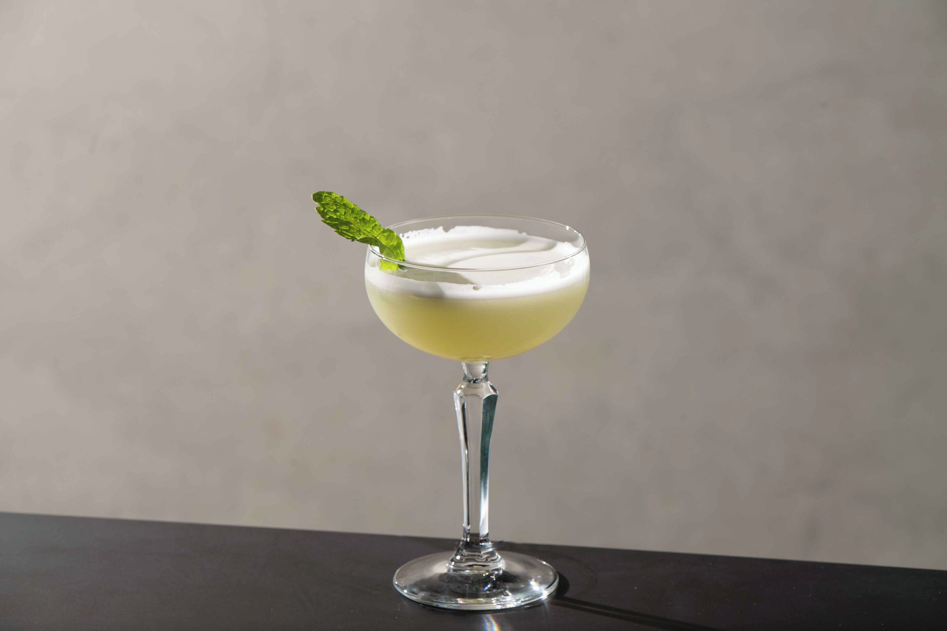 Un cocktail servi dans un verre à pied, décoré d’une feuille de menthe.