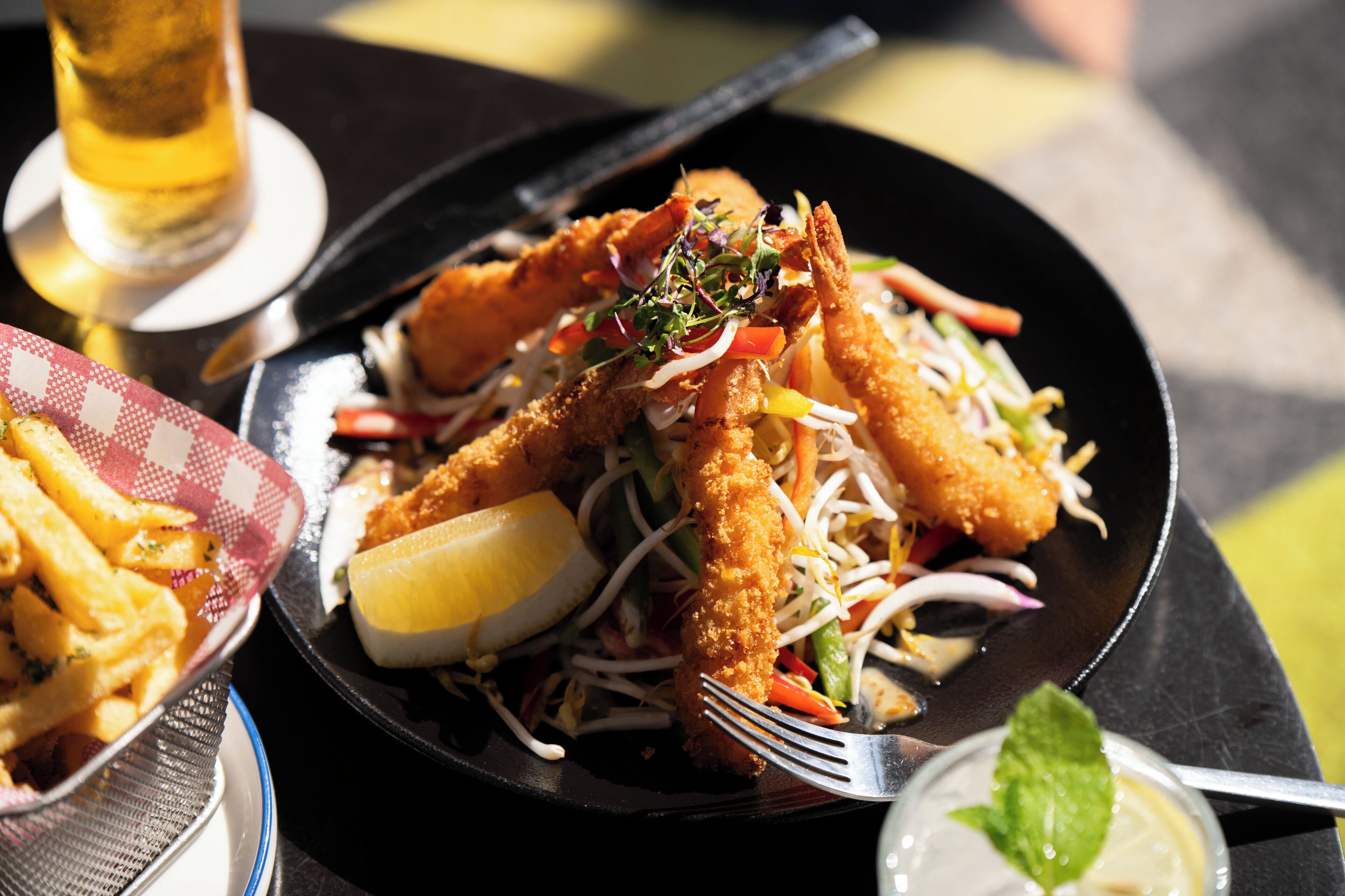 A plate of food with breaded shrimp and vegetables, a lemon wedge, and a mint leaf garnish.
