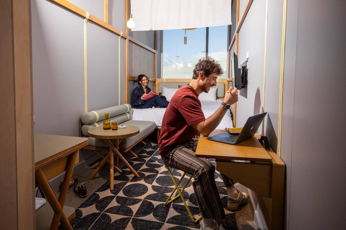 A compact hotel room with a bed, a desk with a laptop, a small round table, and a sofa.