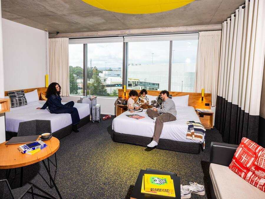 Habitación de hotel con dos camas, un escritorio, una silla y vistas a la ciudad.