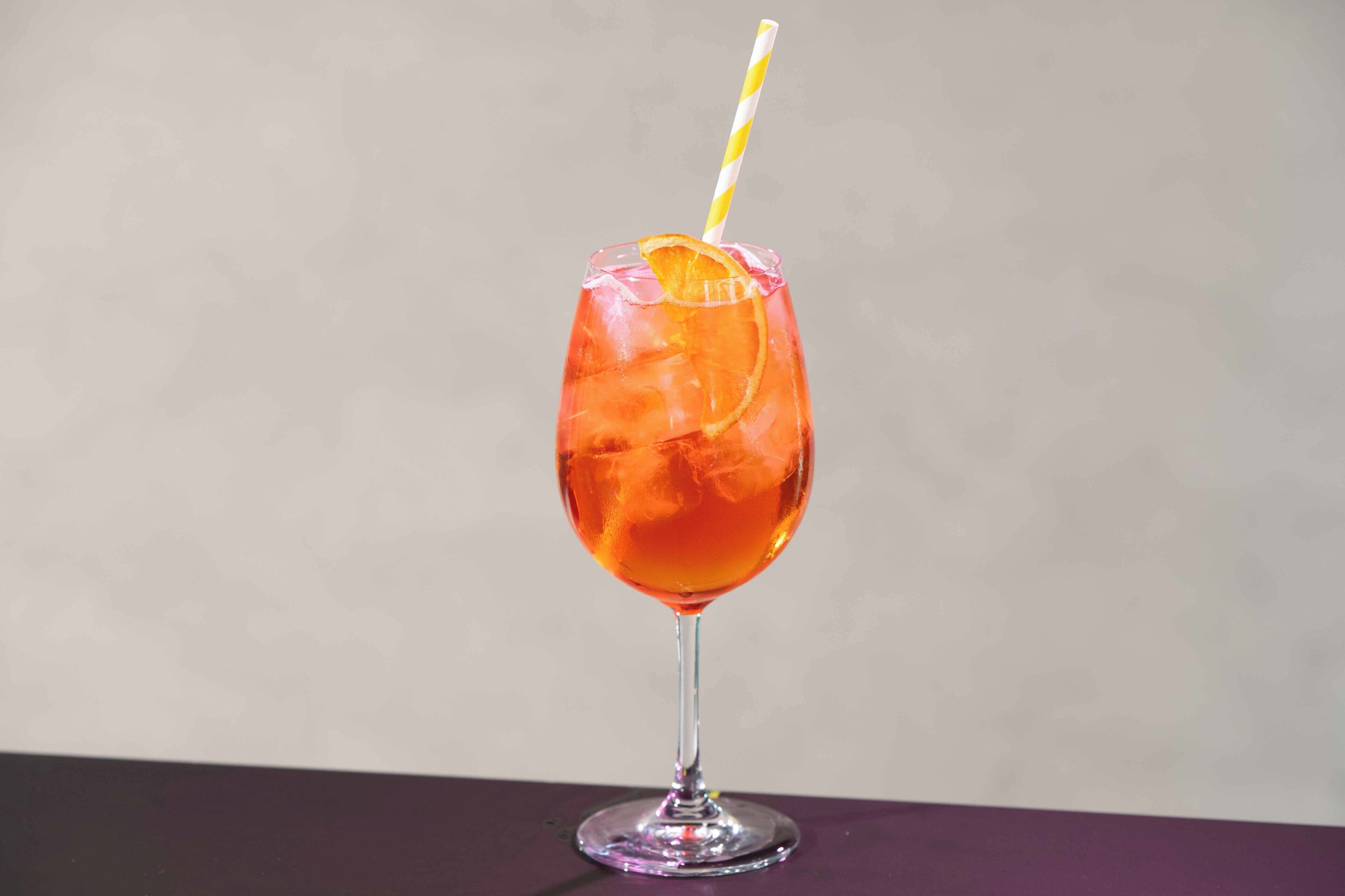 A cocktail glass with a straw and an orange slice on a table.