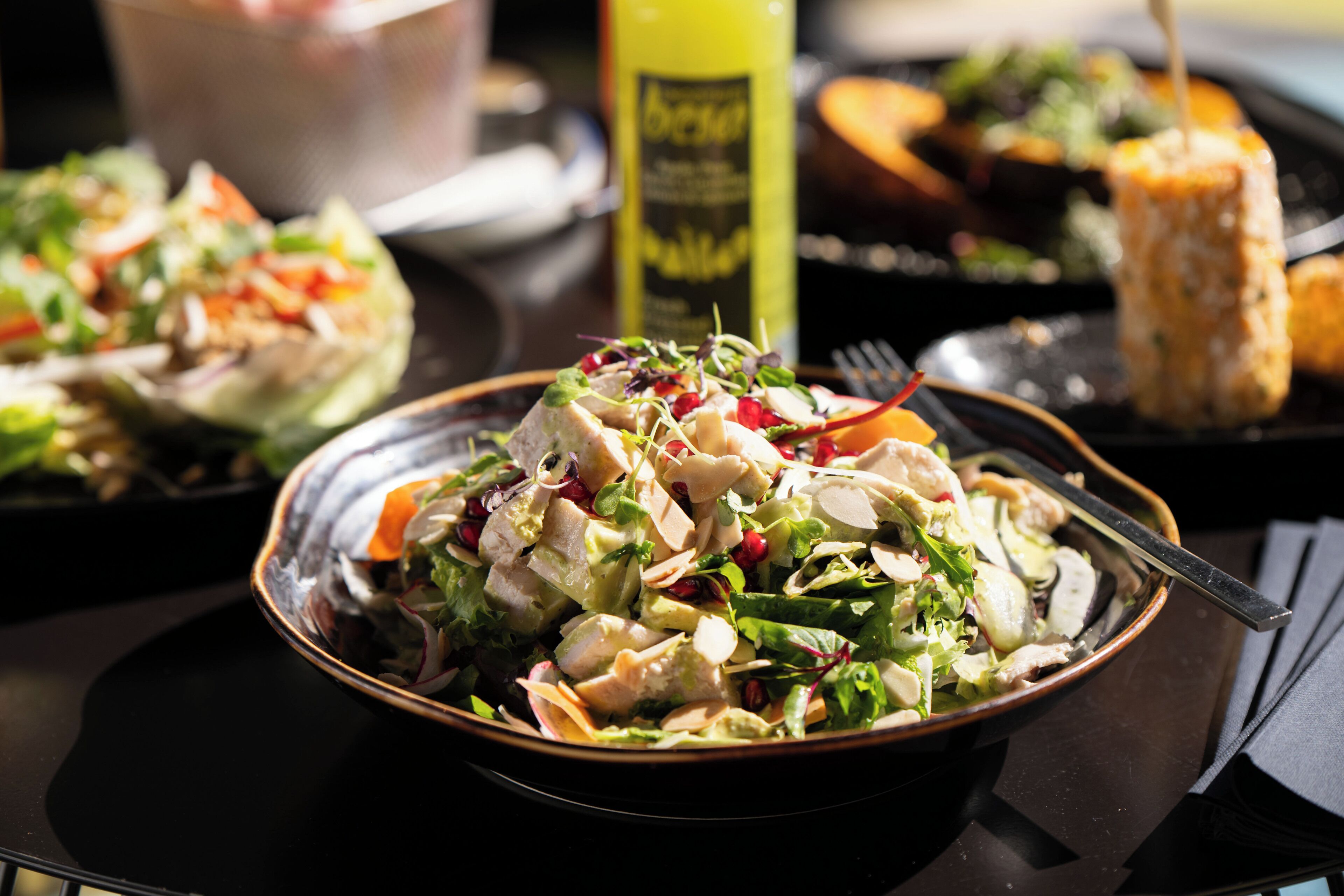 A bowl of salad with various vegetables and a bottle of dressing in the background.