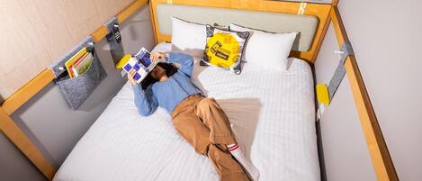 A person lying on a bed with a window above, reading a book.