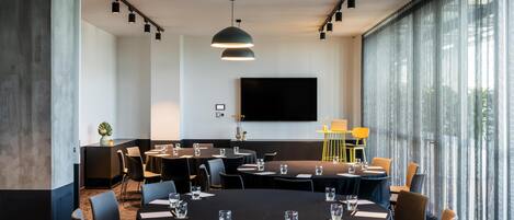 A modern conference room with round tables, chairs, and a large flat-screen TV.