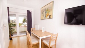 A dining area with a wooden table and chairs, a painting on the wall, and a TV mounted on the wall. - Ferienwohnung BECKENDORF (Losheim am See)