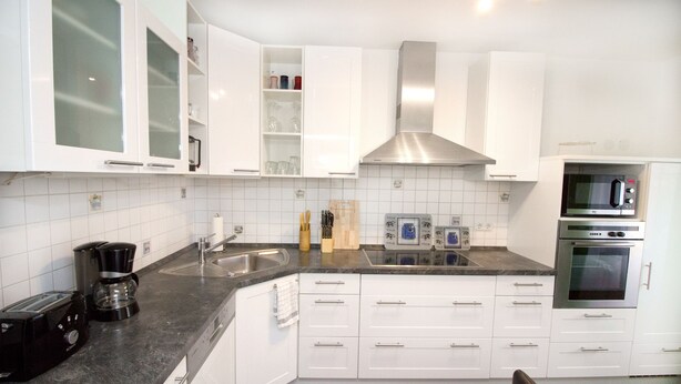 A modern kitchen with white cabinets, a stainless steel range hood, a built-in microwave, and a coffee maker. - Ferienwohnung BECKENDORF (Losheim am See)
