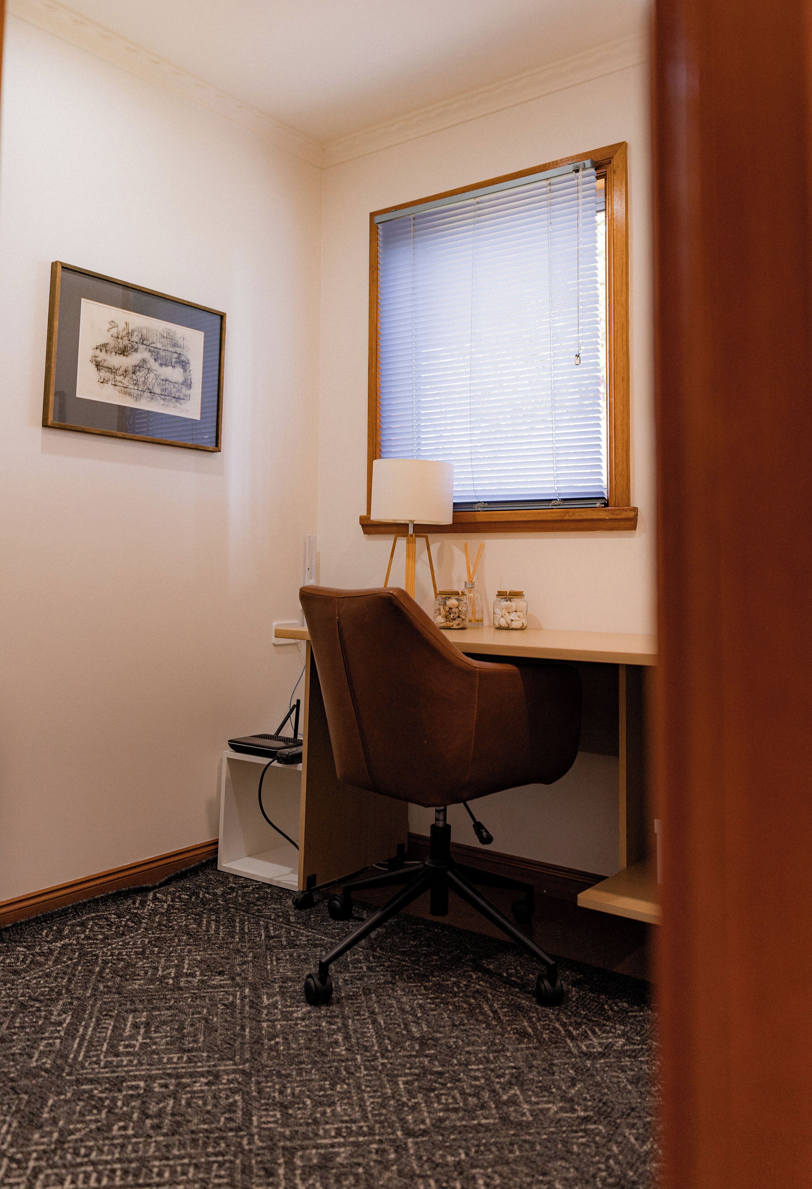 Un bureau d’angle avec un bureau, une chaise, une lampe et un tableau encadré au mur.