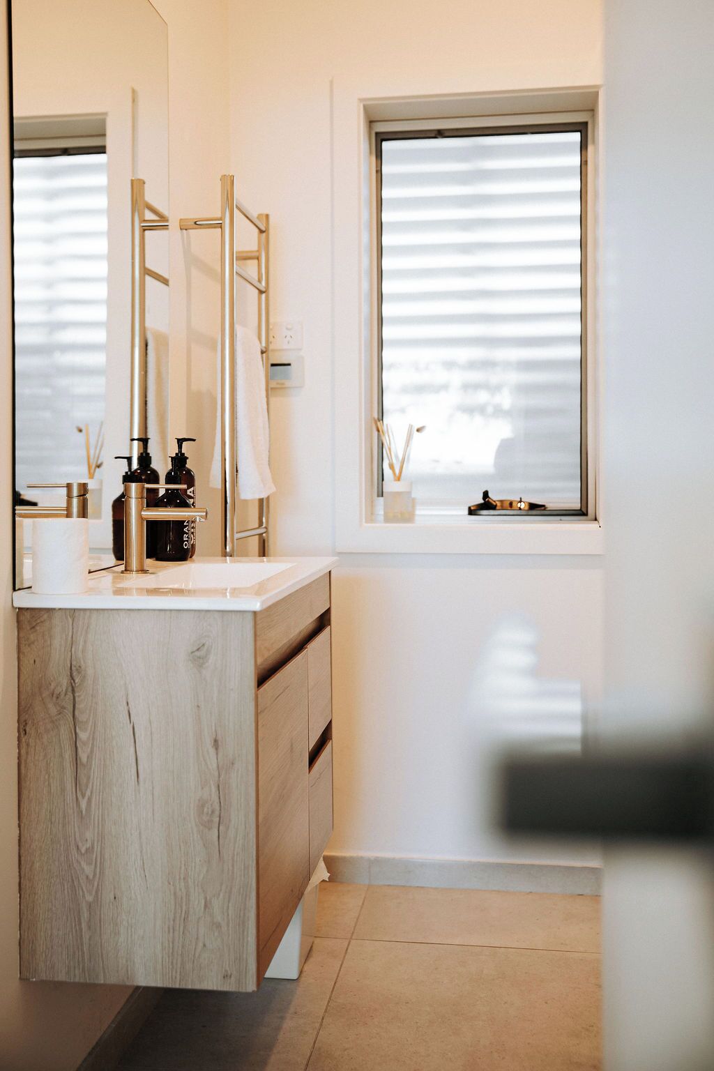 Ein modernes Badezimmer mit einem Holzwaschtisch, einem großen Spiegel und einem Fenster mit Jalousien.