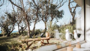 Blick auf eine Terrasse mit Holztisch und -stühlen, umgeben von Bäumen und blauem Himmel.