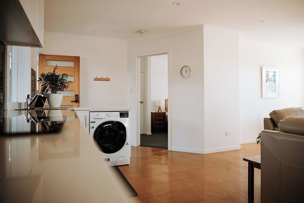 A modern kitchen with a washing machine, a dining area with a sofa, and a living room with a brown carpet.