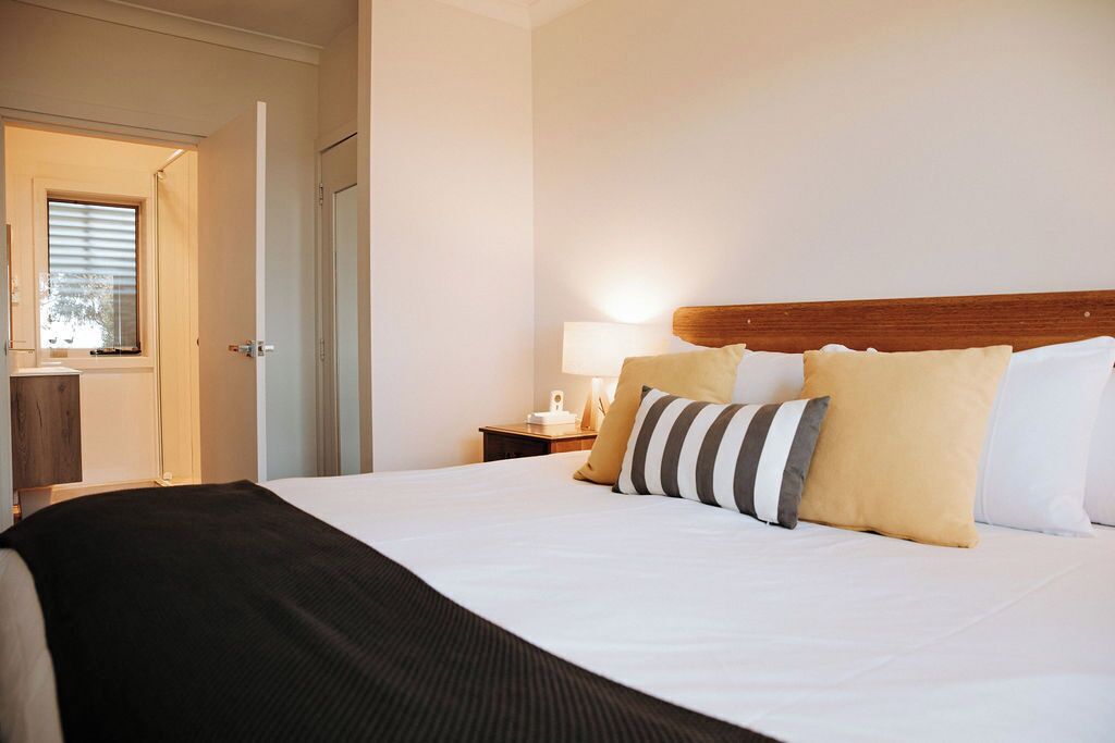 A hotel room with a large bed, a bedside table with a lamp, and a window with blinds.