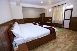 Una cama doble con ropa de cama blanca y una manta a rayas, un armario de madera, una mesita con una lámpara y una ventana con cortinas.