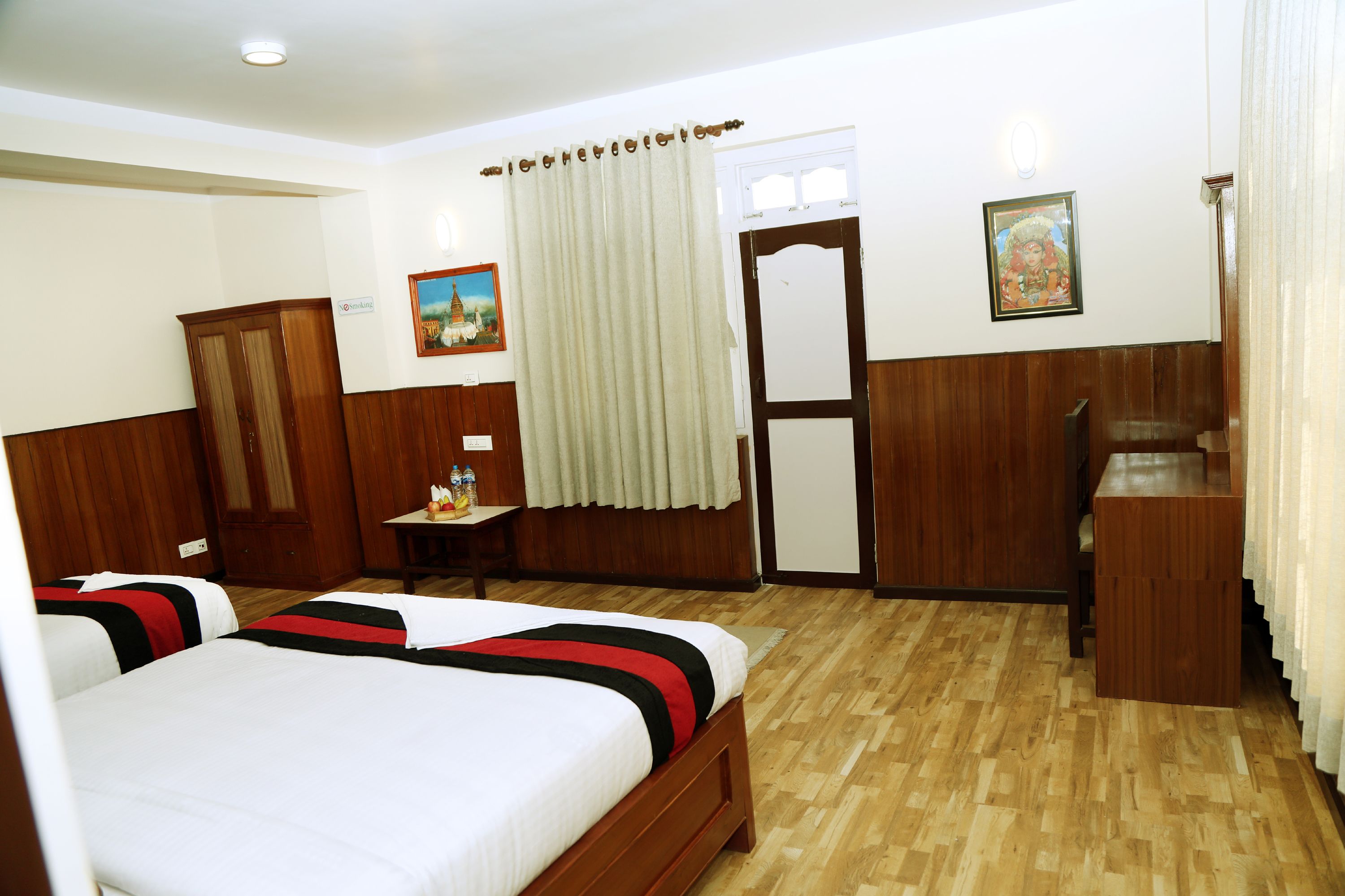 Habitación de hotel con dos camas, suelo de madera, escritorio, armario y una puerta con cortina.