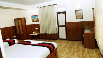 Habitación de hotel con dos camas, suelo de madera, escritorio, armario y una puerta con cortina.