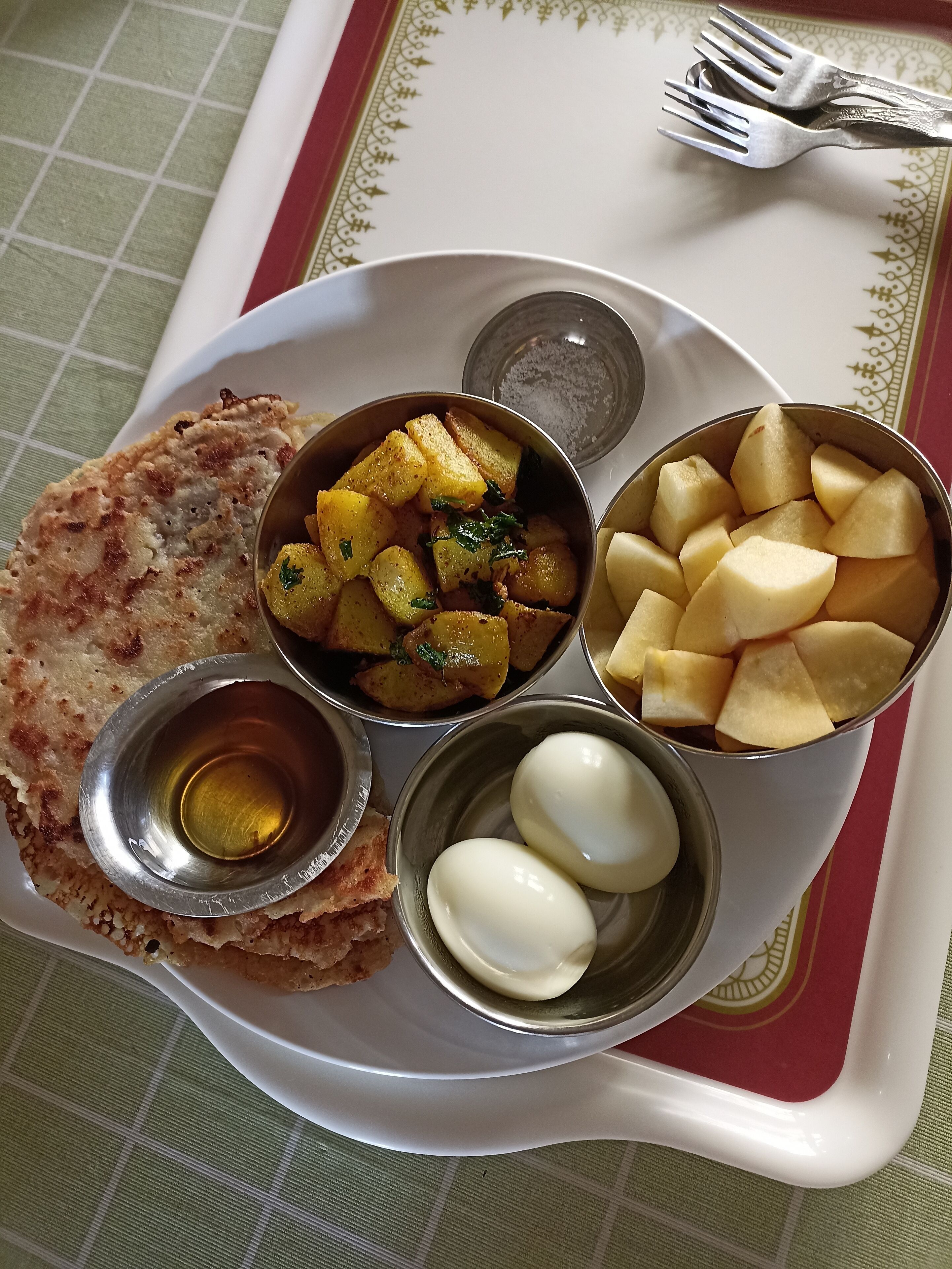 A meal consisting of a flatbread, a bowl of potato curry, a bowl of sliced potatoes, and two boiled eggs on a tray.