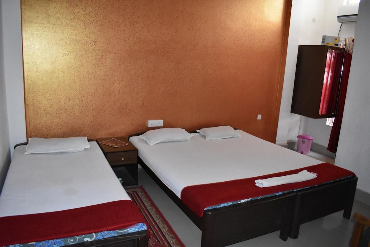 A hotel room with two single beds, a wooden nightstand, a red throw blanket on one bed, and a pink trash bin.