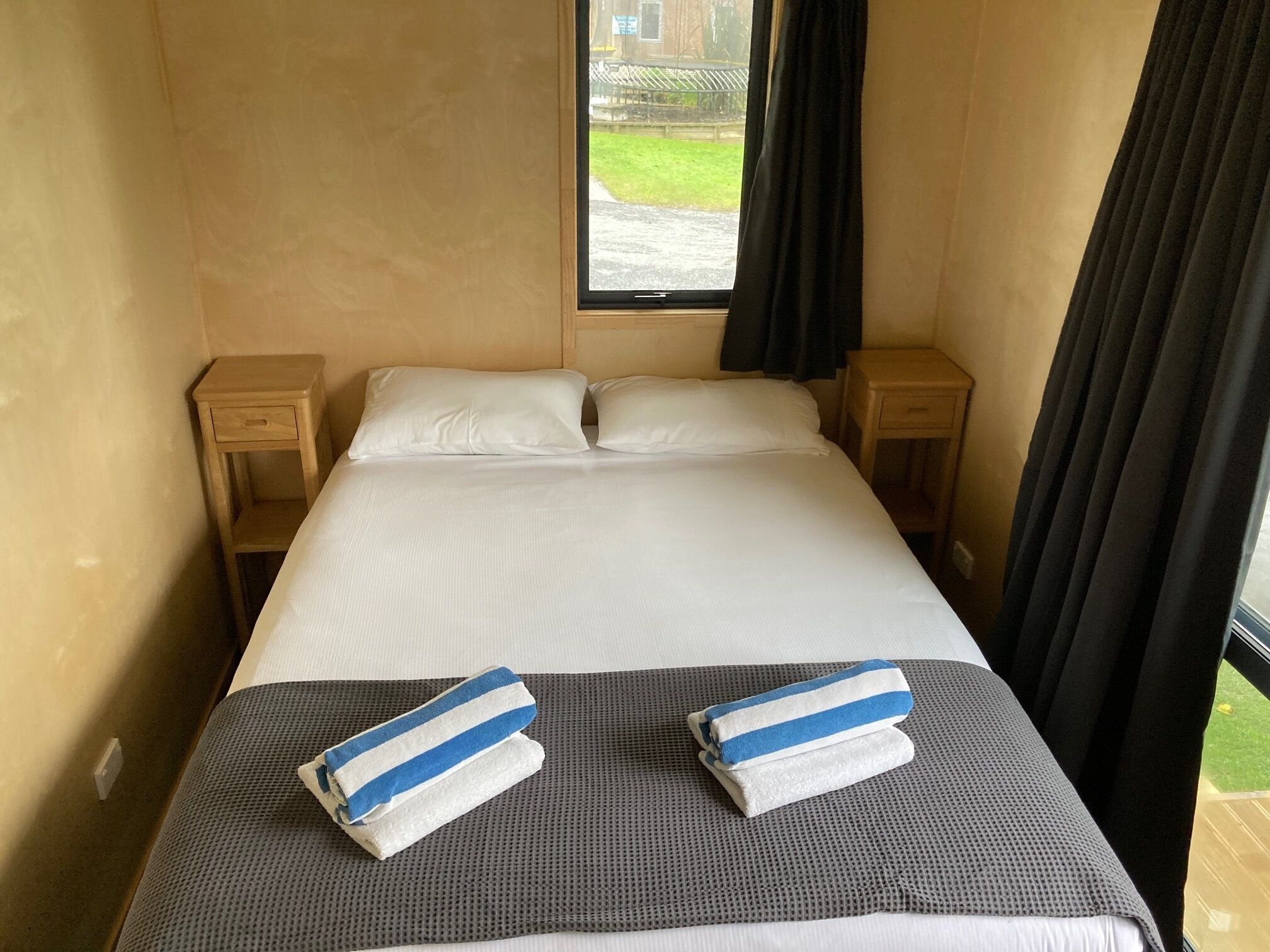 Ein Hotelzimmer mit einem Bett, zwei Nachttischen, einem Fenster mit Vorhängen und Blick ins Freie.