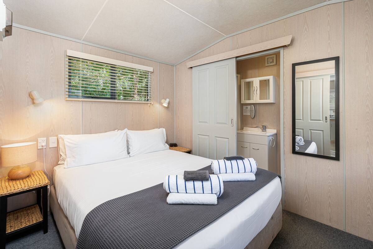 Habitación de hotel ordenada con cama, mesitas de noche, ventana con persianas, espejo y armario.