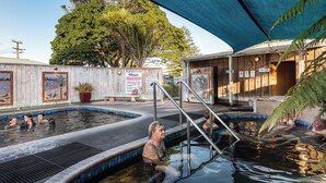 A swimming pool area with a wooden fence, a covered seating area, and a sign indicating 'Aloha Reef'. - Athenree Hot Springs & Holiday Park (Waihi Beach)