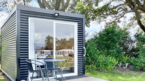 A modern, compact cabin with a deck and outdoor seating area. - Athenree Hot Springs & Holiday Park (Waihi Beach)