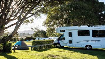 A white RV parked in a grassy area with a tent nearby.