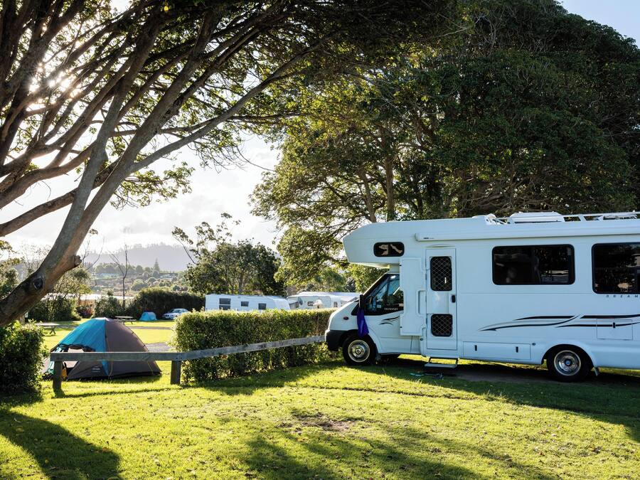 A white RV parked in a grassy area with a tent nearby.