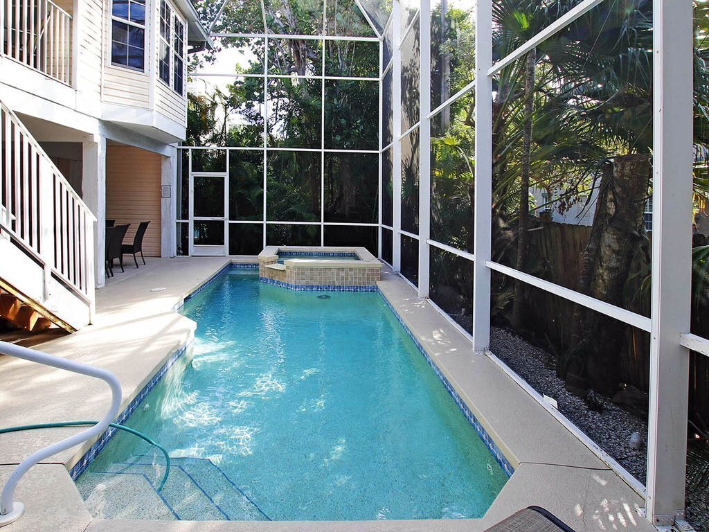 Una piscina rectangular con borde de azulejos, rodeada por una valla blanca y paneles de vidrio, con una escalera que conduce a un nivel superior.