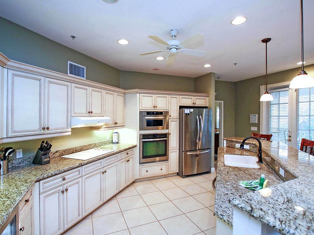 A modern kitchen with white cabinetry, granite countertops, stainless steel appliances, and a ceiling fan.